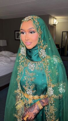 a woman wearing a green veil and headpiece with gold accents on her face, standing in front of a bed