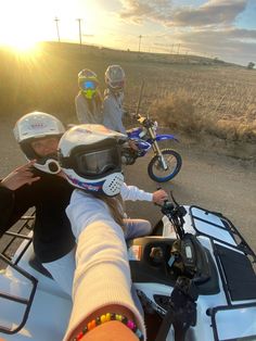 three people riding on the back of a motorcycle down a country road at sundown