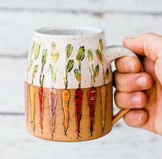 a hand holding a coffee mug with carrots painted on the outside and inside it