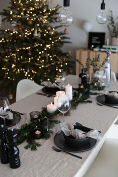 the table is set with black and white dishes, candles, and christmas tree in the background