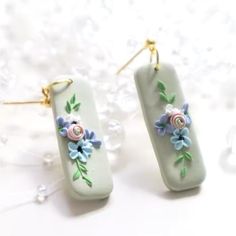 two earrings with flowers on them sitting on top of a white table next to bubbles