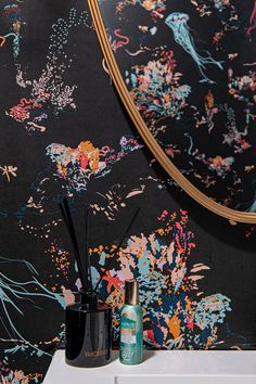 a mirror and some vases on a table in front of a floral wallpaper