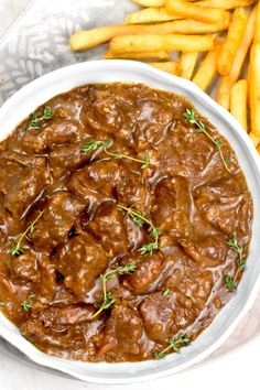 a white bowl filled with meat and gravy next to french fries