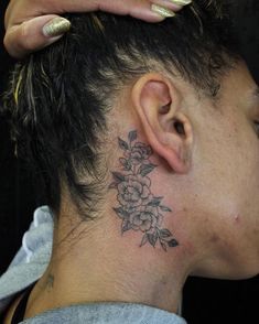 a woman with a flower tattoo on her neck and behind her ear is looking at the camera