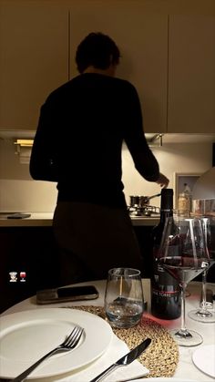 a person standing over a table with plates and wine glasses on it in front of a bottle