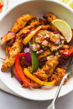 a white bowl filled with chicken fajita and vegetables next to a lemon wedge