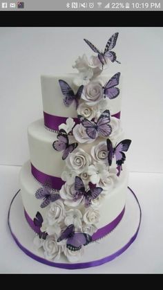 a three tiered cake with purple and white flowers on the top, and butterflies on the side