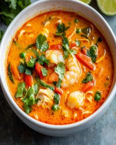 a white bowl filled with shrimp and vegetables next to cilantro, lime wedges