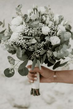 a person holding a bouquet of flowers in their hand on the beach with sand behind them