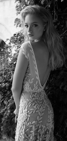 black and white photograph of a woman in a dress standing next to a wall with vines