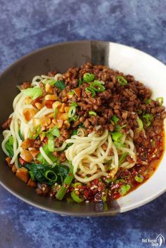 a bowl filled with noodles and meat on top of a blue countertop next to a fork