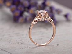 a pink diamond ring sitting on top of a piece of paper next to purple flowers