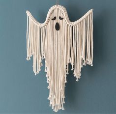 a white hanging decoration with black eyes and fringes on it's face, in front of a blue wall