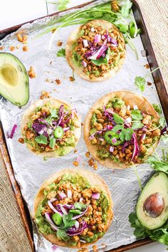 four tacos on a baking sheet with avocado and cilantro