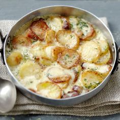 a silver pan filled with potatoes on top of a cloth next to a spoon and fork