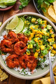 a bowl filled with shrimp and rice next to tortilla chips, lime wedges and avocado