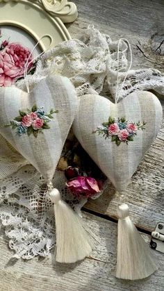 two hearts with flowers and tassels are on a table next to lace doily