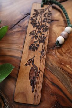 a wooden bookmark with two birds on it sitting on a table next to some green leaves