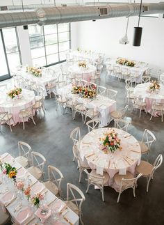 tables and chairs are set up for a wedding reception in an industrial setting with large windows