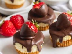 three cupcakes with chocolate frosting and strawberries on the plate next to them