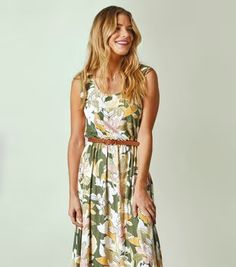 a woman standing in front of a white wall wearing a dress with flowers on it