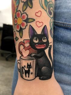 a black cat holding a coffee cup with hearts on it's arm and paw