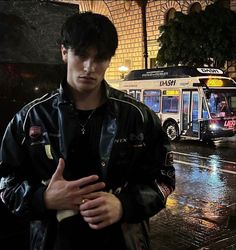 a young man standing in front of a bus on a rainy night with his hand up to his chest