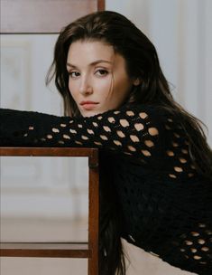 a woman leaning on a chair with her arms crossed and looking at the camera while wearing a black sweater