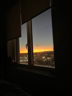 the sun is setting over a city seen from a window in a room with dark walls