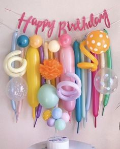 a birthday cake with balloons and streamers hanging from it's side, next to a sign that says happy birthday