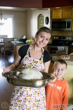 a woman standing next to a little boy holding a pan with food on top of it