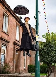 a statue of a woman holding an umbrella on a lamp post in front of a building