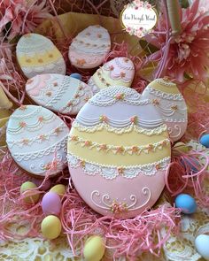 some decorated cookies in a basket with pink and yellow eggs around them on a table