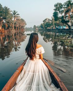 a woman in a white dress is sitting in a boat on the water with palm trees