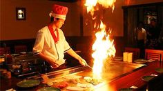 a man cooking food on top of a grill in front of a large sign that says om