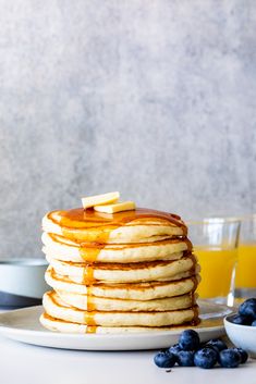 a stack of pancakes with syrup and blueberries on a plate next to glasses of orange juice