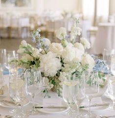 the table is set with white and blue flowers in vases, wine glasses, and silverware