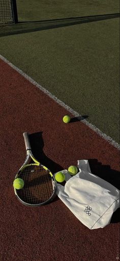 a tennis racket and ball laying on the ground next to a white bag with yellow balls in it