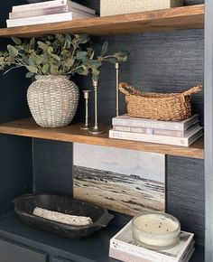 a shelf with books, vases and other items on it in a room that has dark blue walls