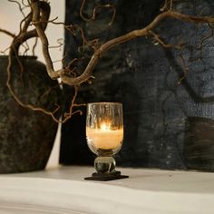 a lit candle sitting on top of a mantle next to two vases with branches