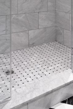 a walk in shower sitting next to a white tiled wall and floor with black dots on it