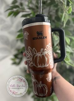 a person holding up a coffee cup with pumpkins on the side and leaves around it