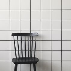 a black chair sitting in front of a white tiled wall with a wooden seat on it