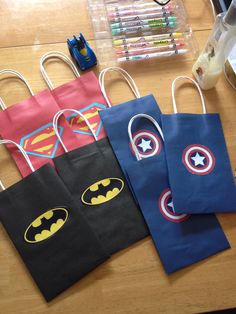 three bags with batman and superman logos on them sitting on a table next to markers