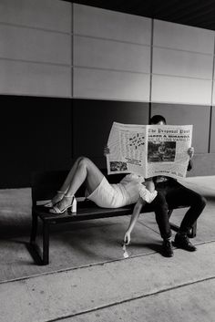 a man and woman sitting on a bench reading newspapers