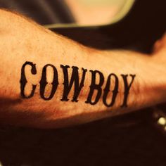 a man's arm with the word cowboy tattooed on it, in black ink