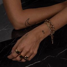 a woman with tattoos on her arm and wrist is sitting down wearing gold bracelets