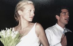 a man standing next to a woman in a white dress holding a bouquet of flowers