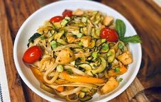 a white bowl filled with noodles and vegetables on top of a wooden table next to another bowl