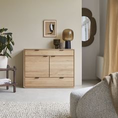 a living room with a chair, dresser and potted plant on the sideboard